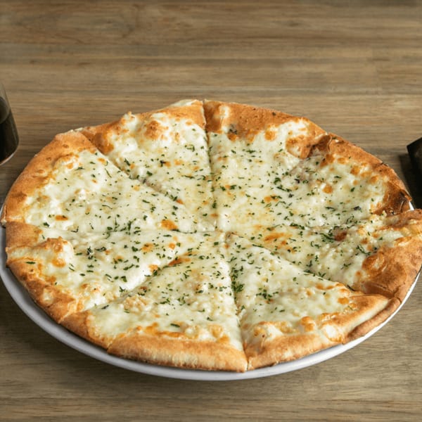 A round, sliced garlic cheese pizza with parsley flakes on a white plate and wooden table.