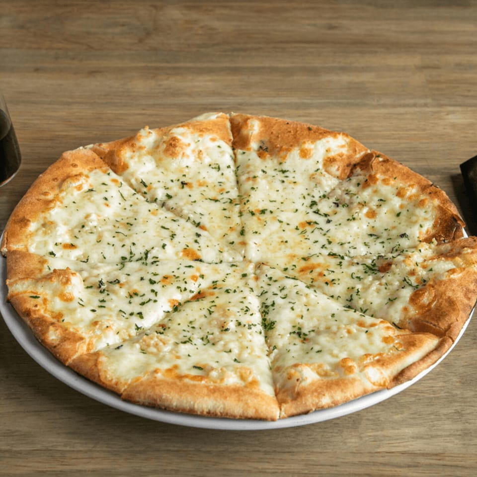 A round, sliced garlic cheese pizza with parsley flakes on a white plate and wooden table.