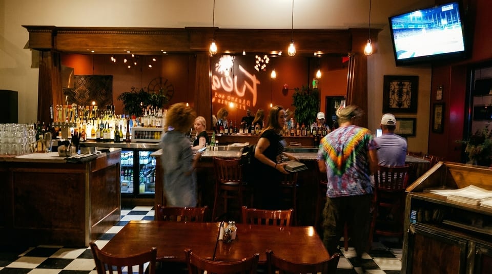 A lively bar scene with patrons, a well-stocked bar, and a television showing a game.
