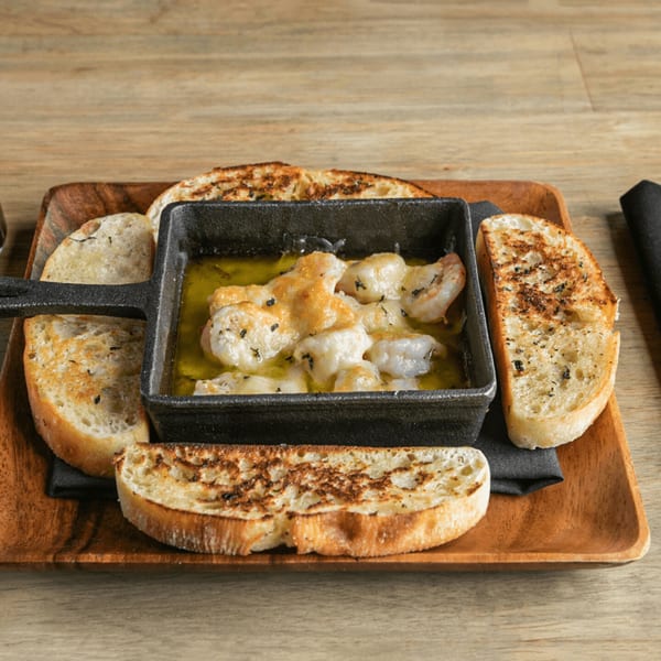 Shrimp scampi in a cast iron dish with toasted bread slices on a wooden tray.