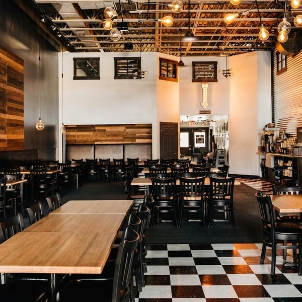 Spacious Fuego Bistro and Pizzeria dining room with wooden tables, black chairs, and checkered floors.