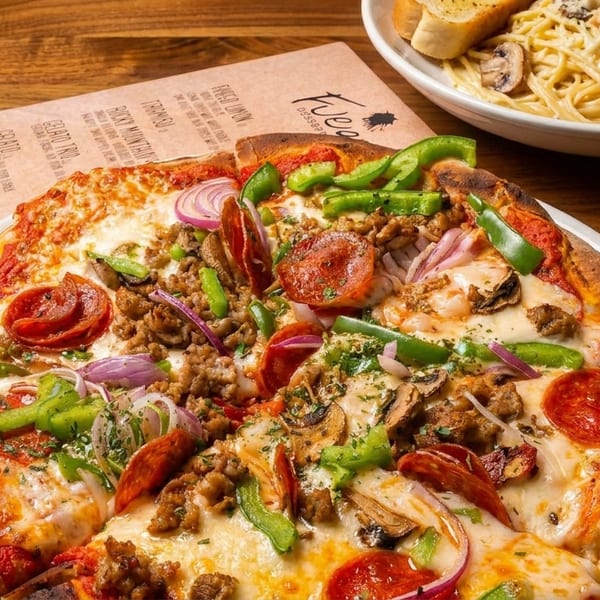 A Fuego pizza with pepperoni, sausage, peppers, onions, and mushrooms, alongside pasta and garlic bread.