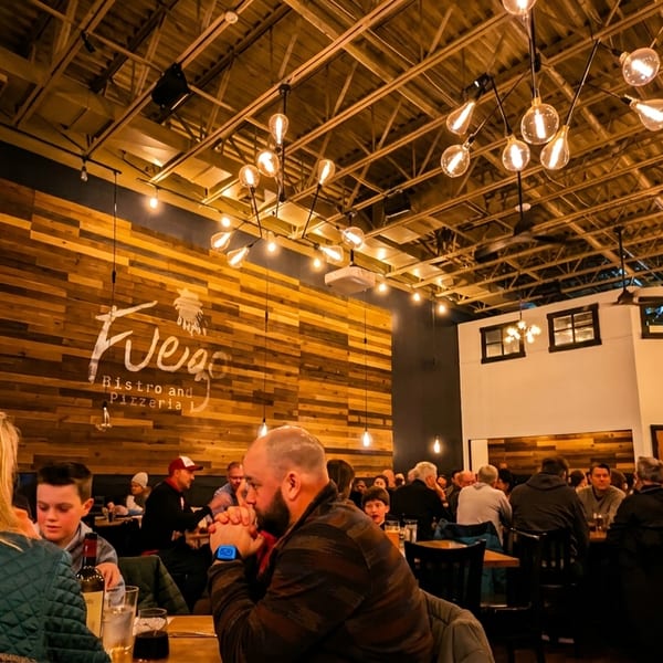 Diners seated at tables in a dimly lit restaurant with a wooden accent wall and industrial lighting.