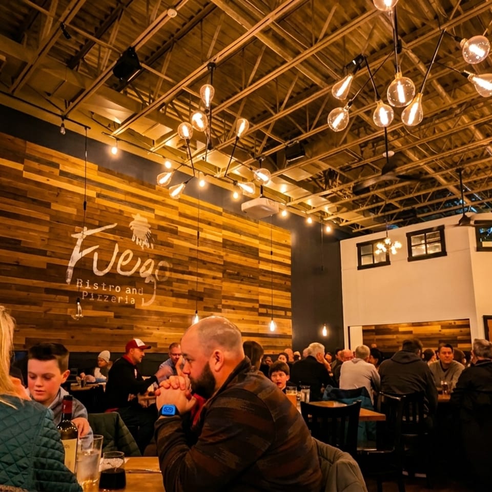 Diners seated at tables in a dimly lit restaurant with a wooden accent wall and industrial lighting.