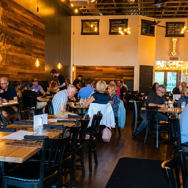 A bustling restaurant interior with patrons dining at tables and a large Fuego Bistro & Pizzeria sign.