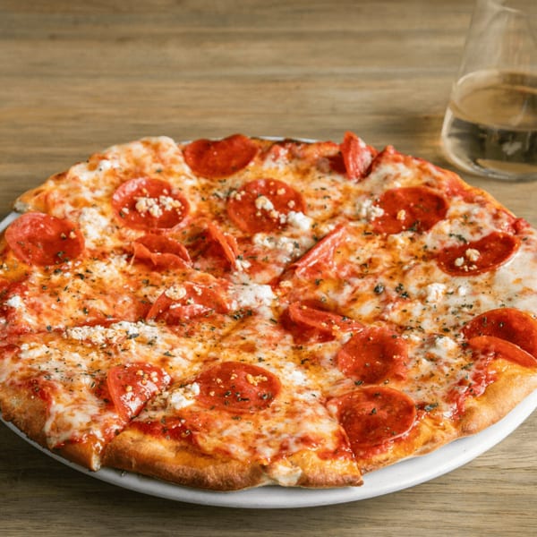 Pepperoni pizza with melted cheese, herbs, and feta crumbles on a white plate with a drink.