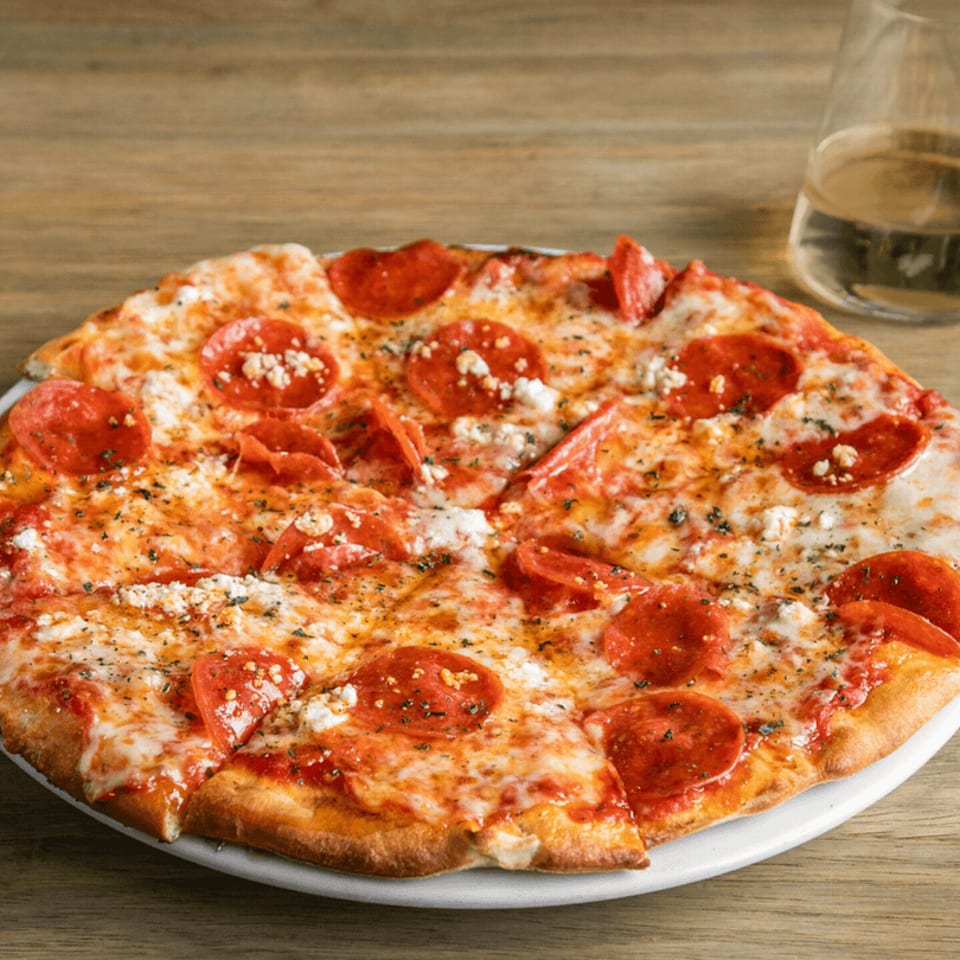 Pepperoni pizza with melted cheese, herbs, and feta crumbles on a white plate with a drink.