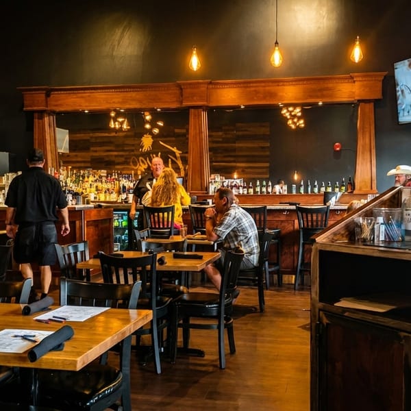 Restaurant interior with wooden tables, a bar with patrons, and a server walking through the dining area.