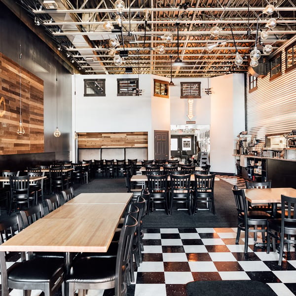 Spacious Fuego Bistro and Pizzeria interior with black and white checkered floor, wooden tables, and black chairs.