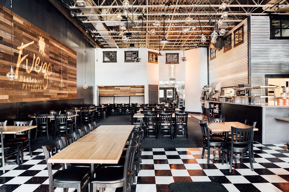 Spacious Fuego Bistro and Pizzeria interior with black and white checkered floor, wooden tables, and black chairs.
